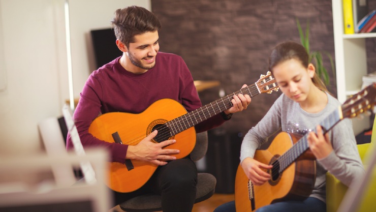 Guru musik tengah mengajarkan muridnya bermain Gitar (Shutterstock).