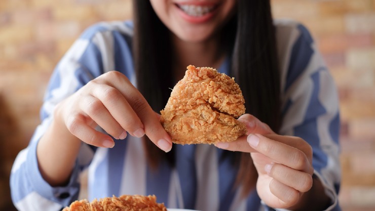 Seorang perempuan tengah makan ayam goreng (Shutterstock).